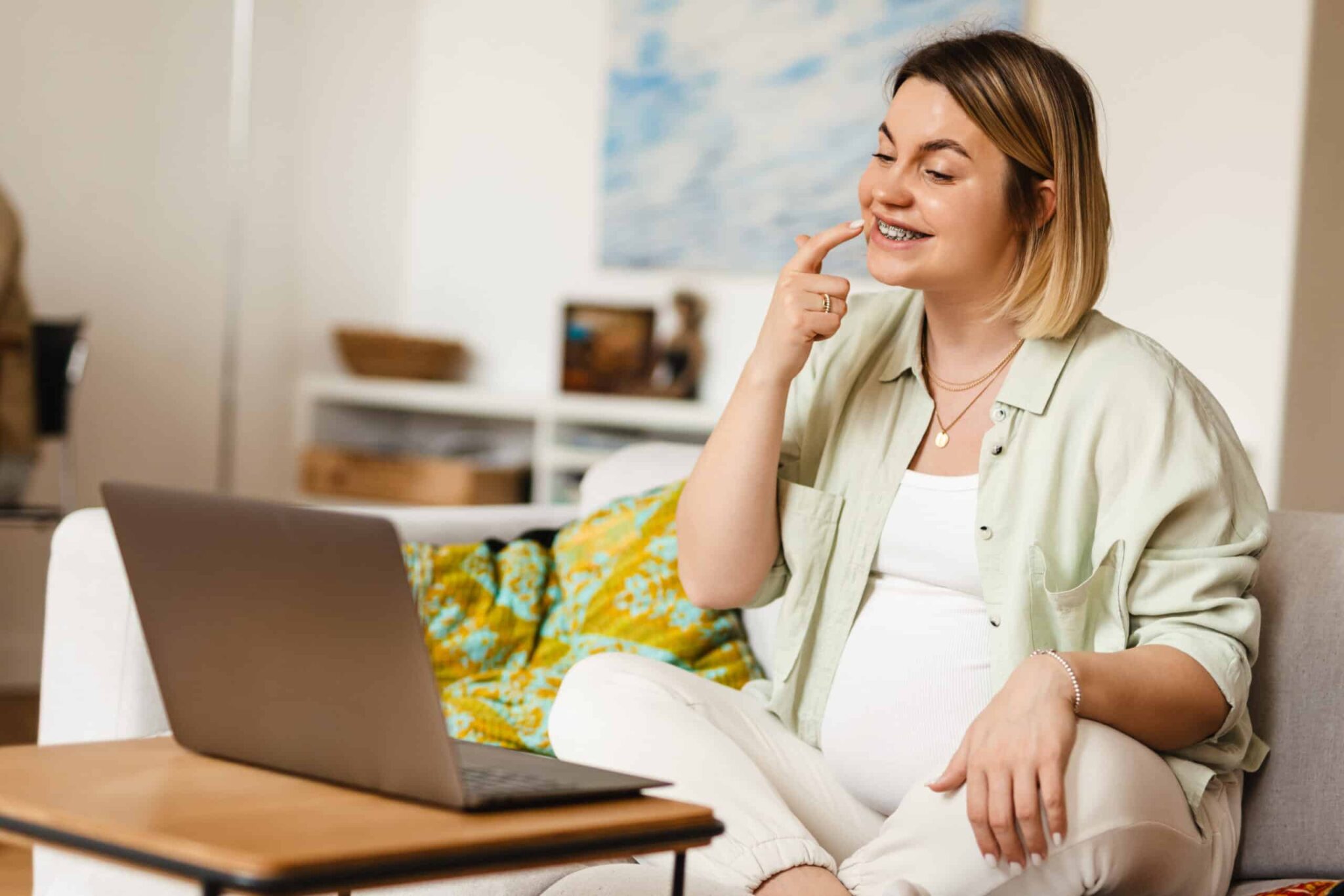 young pregnant woman using laptop while sitting on couch at home